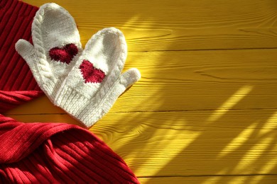 Red knitted scarf and mittens on yellow wooden table, top view. Space for text