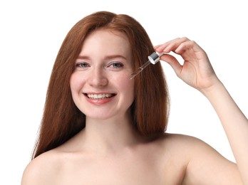 Smiling woman with freckles applying cosmetic serum onto her face against white background