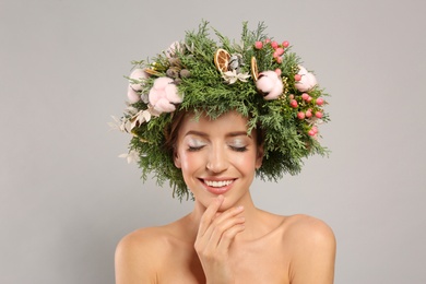 Happy young woman wearing wreath on grey background