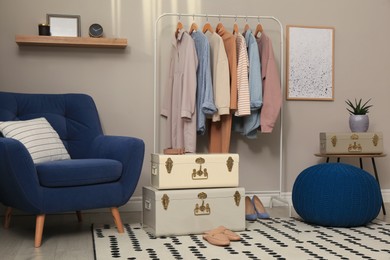 Photo of Stylish room interior with comfortable armchair, clothes and storage trunks