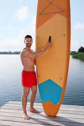 Photo of Man standing near SUP board on pier