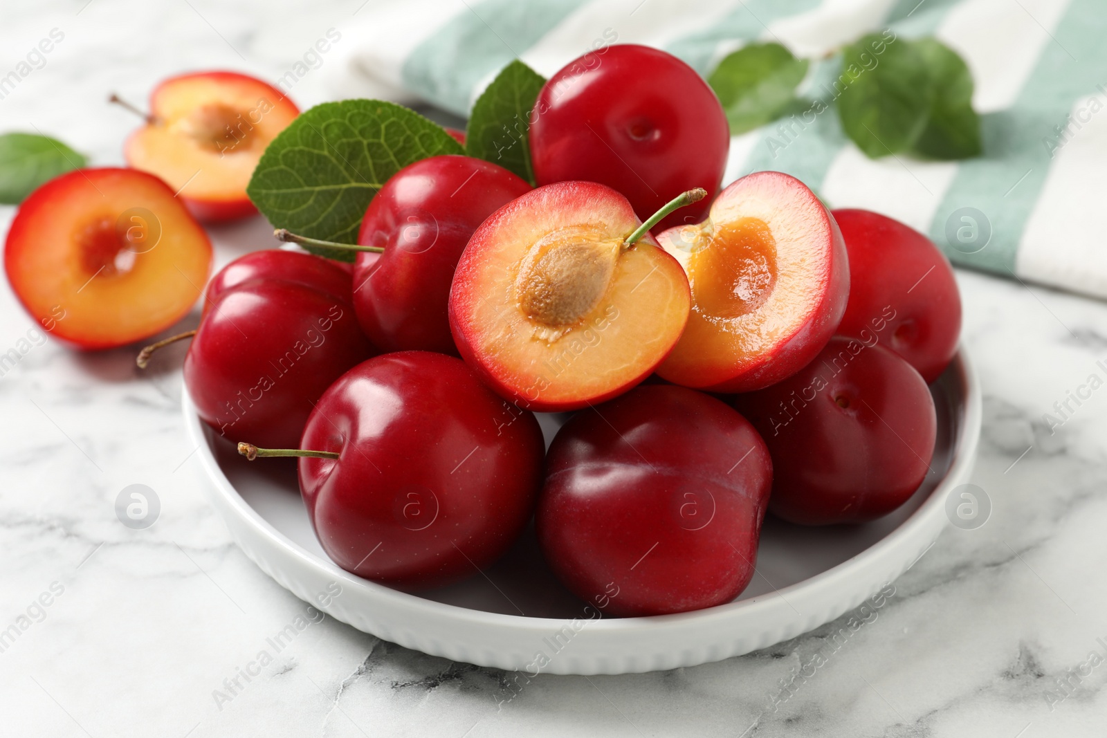 Photo of Delicious ripe cherry plums with leaves on white marble table