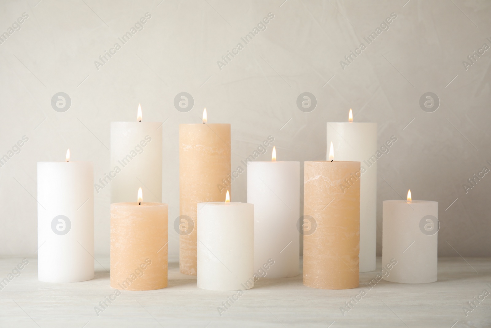 Photo of Burning candles on table against light background