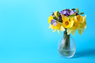 Photo of Bouquet of beautiful yellow daffodils, iris and periwinkle flowers in vase on light blue background, space for text