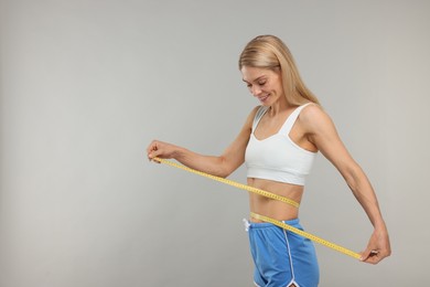 Photo of Slim woman measuring waist with tape on grey background, space for text. Weight loss