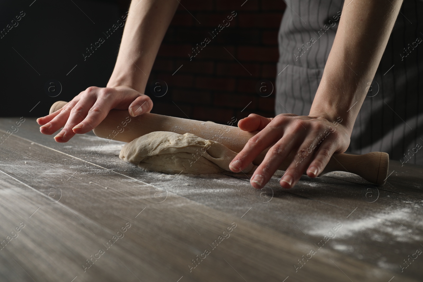 Photo of Making bread. Woman rolling dough at wooden table indoors, closeup