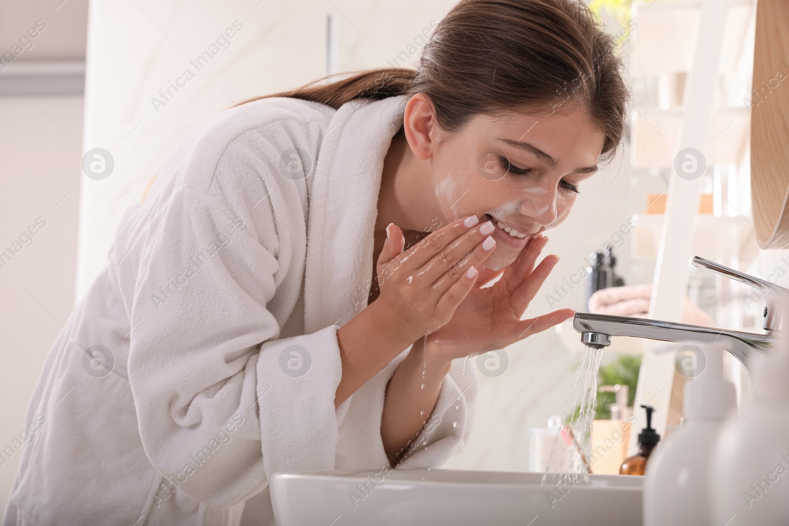 Photo of Beautiful teenage girl washing face with cleansing foam in bathroom. Skin care cosmetic