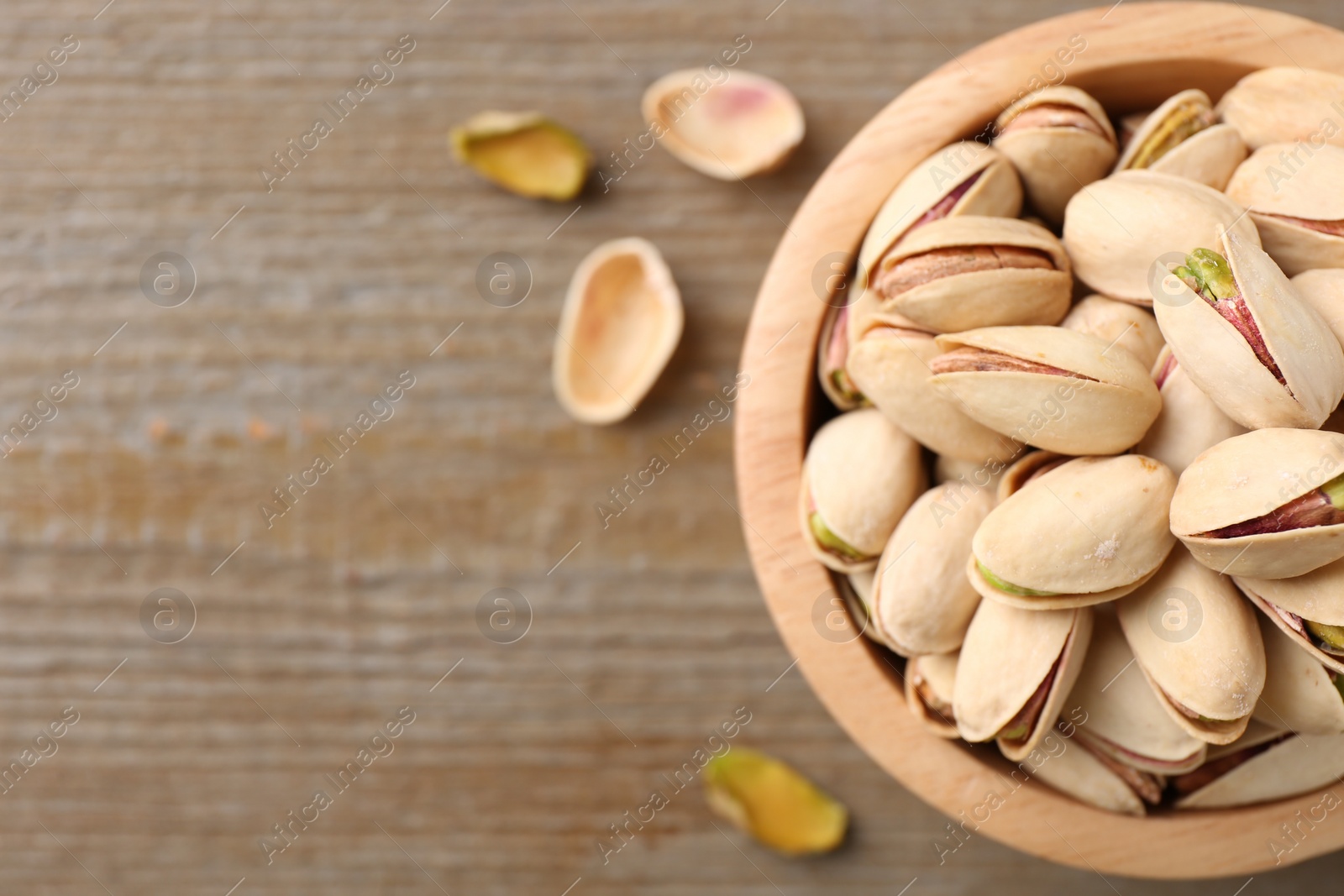 Photo of Tasty pistachios in bowl on wooden table, top view. Space for text