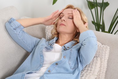 Photo of Woman suffering from headache on sofa at home. Hormonal disorders