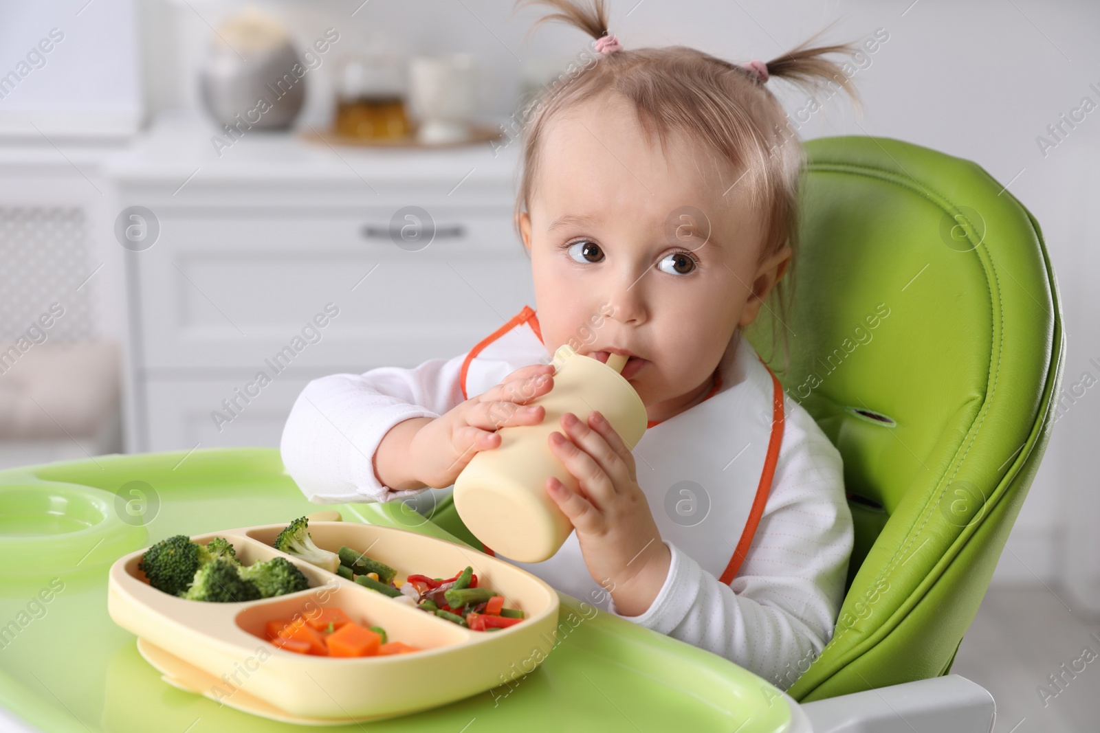 Photo of Cute little baby drinking from bottle in high chair indoors