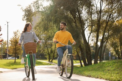 Photo of Beautiful young couple riding bicycles in park, space for text