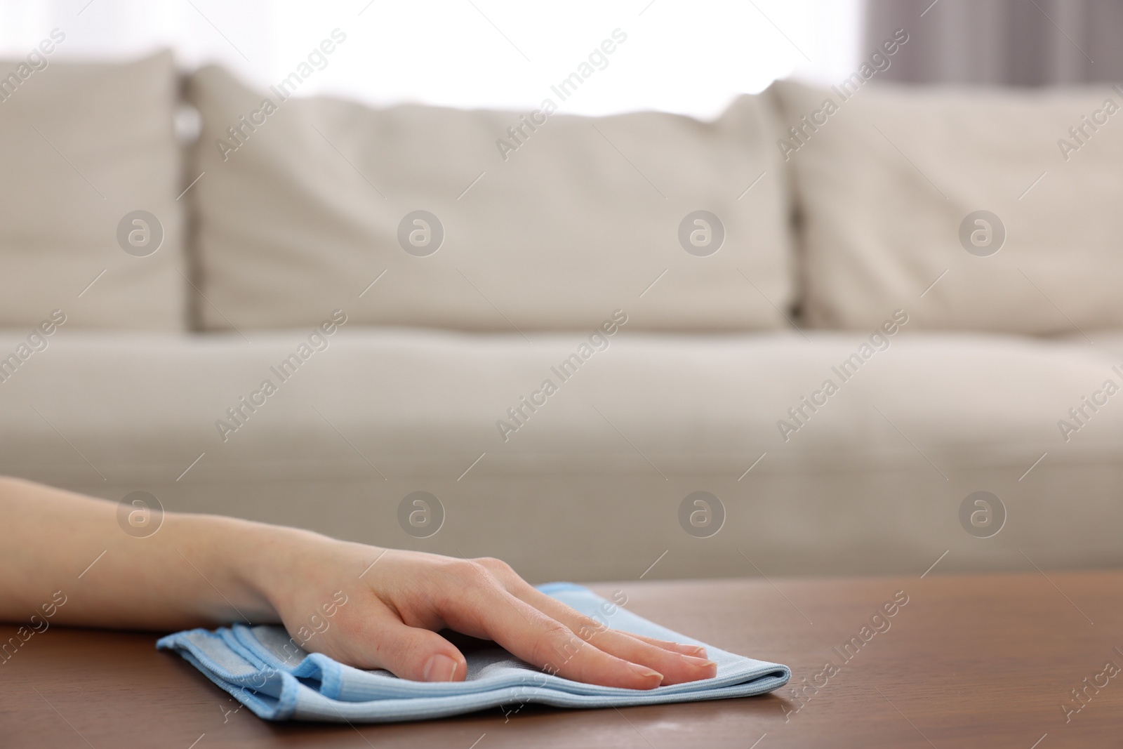 Photo of Woman with microfiber cloth cleaning wooden table in room, closeup. Space for text