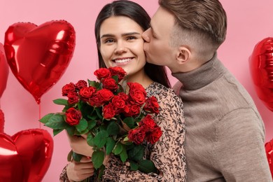 Photo of Happy couple celebrating Valentine's day, beloved woman with bouquetred roses on pink background