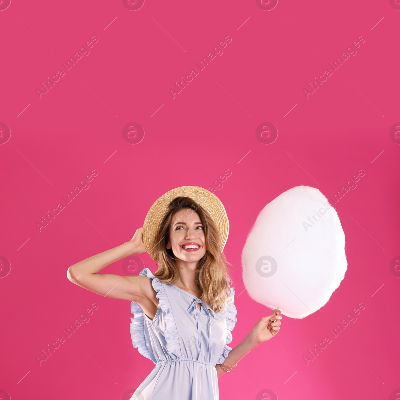 Photo of Happy young woman with cotton candy on pink background