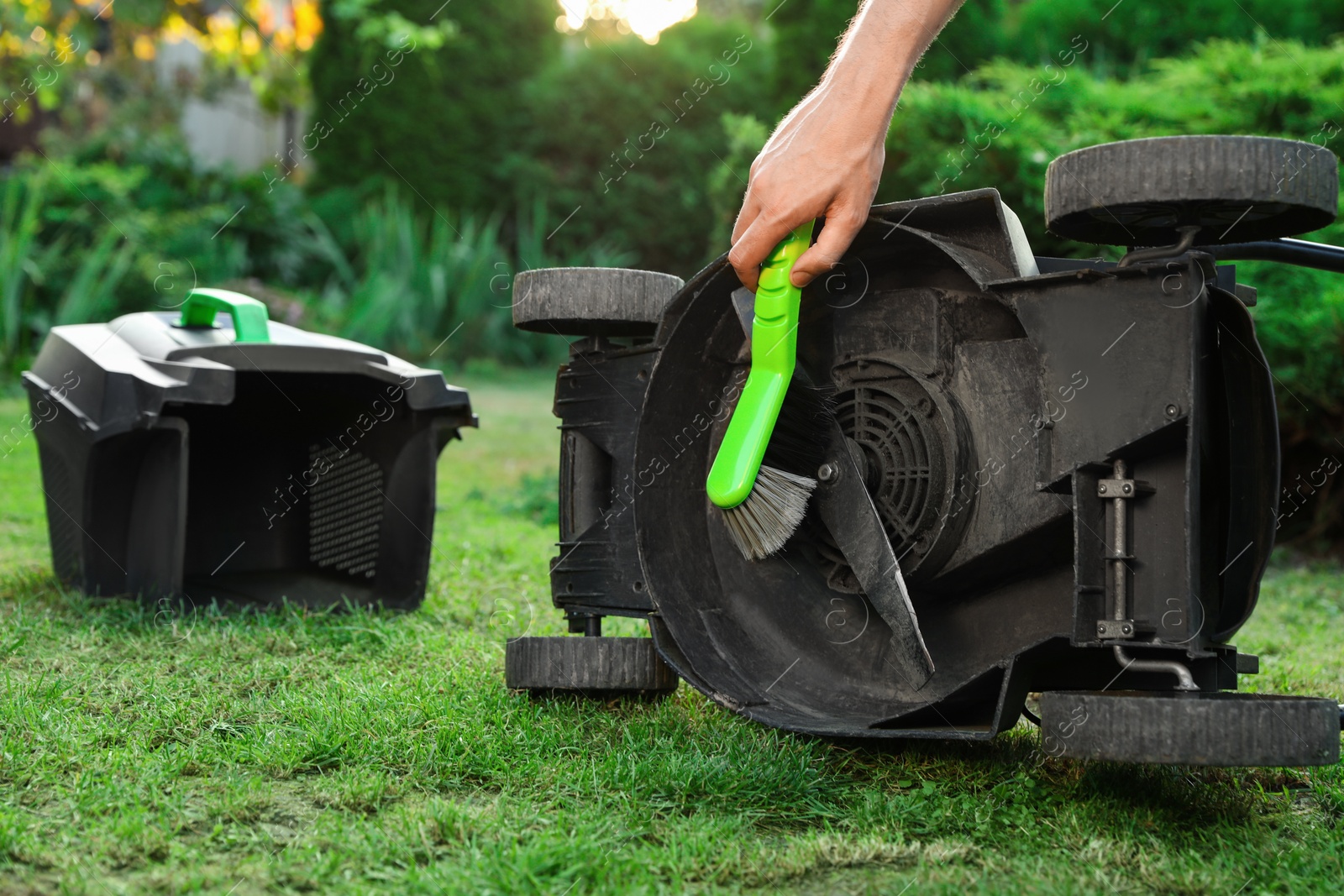 Photo of Man cleaning lawn mower with brush in garden, closeup