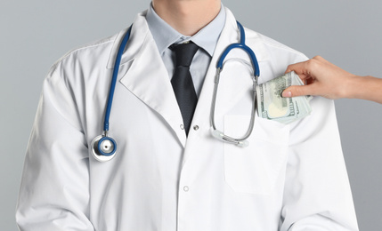 Patient putting bribe into doctor's pocket on grey background, closeup. Corruption in medicine