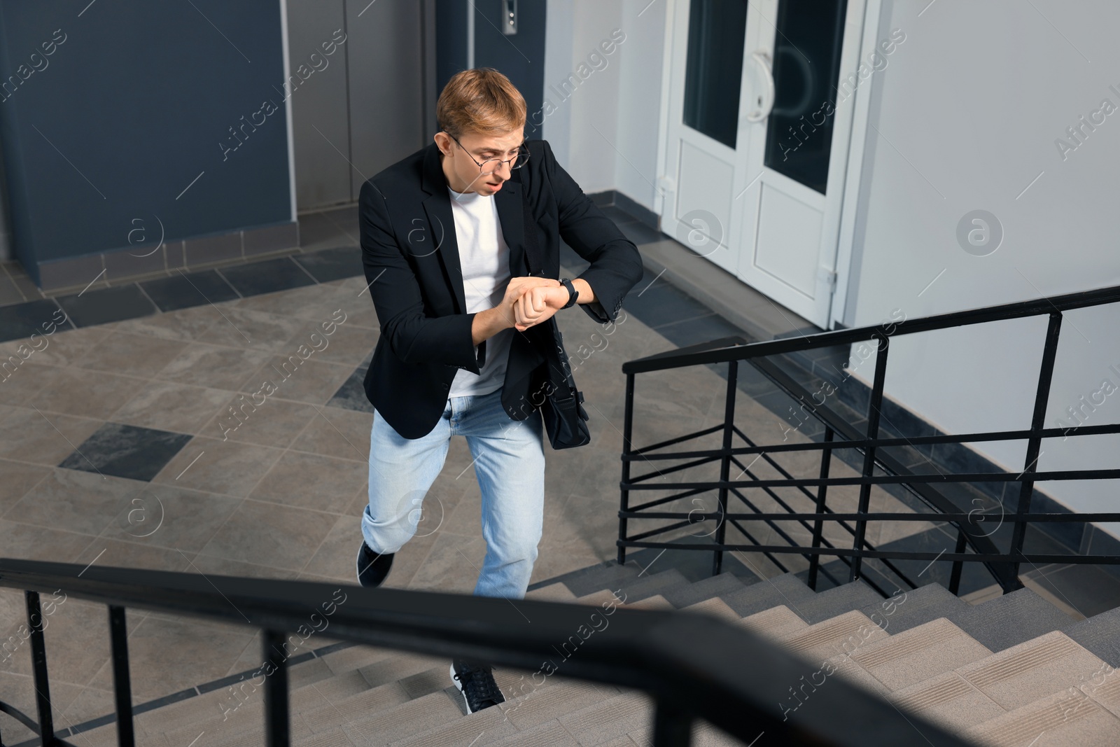 Photo of Emotional man checking time while walking up stairs in office. Being late