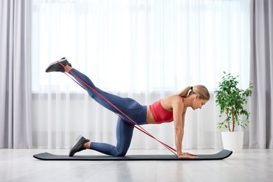 Athletic woman doing exercise with fitness elastic band on mat at home