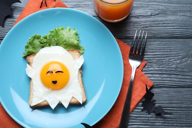 Photo of Halloween themed breakfast served on black wooden table, flat lay. Tasty toast with fried egg in shape of ghost