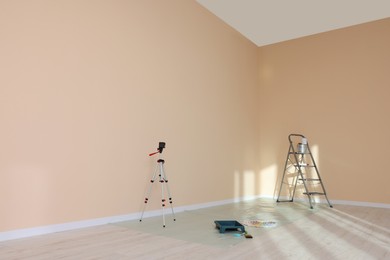Photo of Stepladder, laser level and painting tools near wall in empty room, space for text