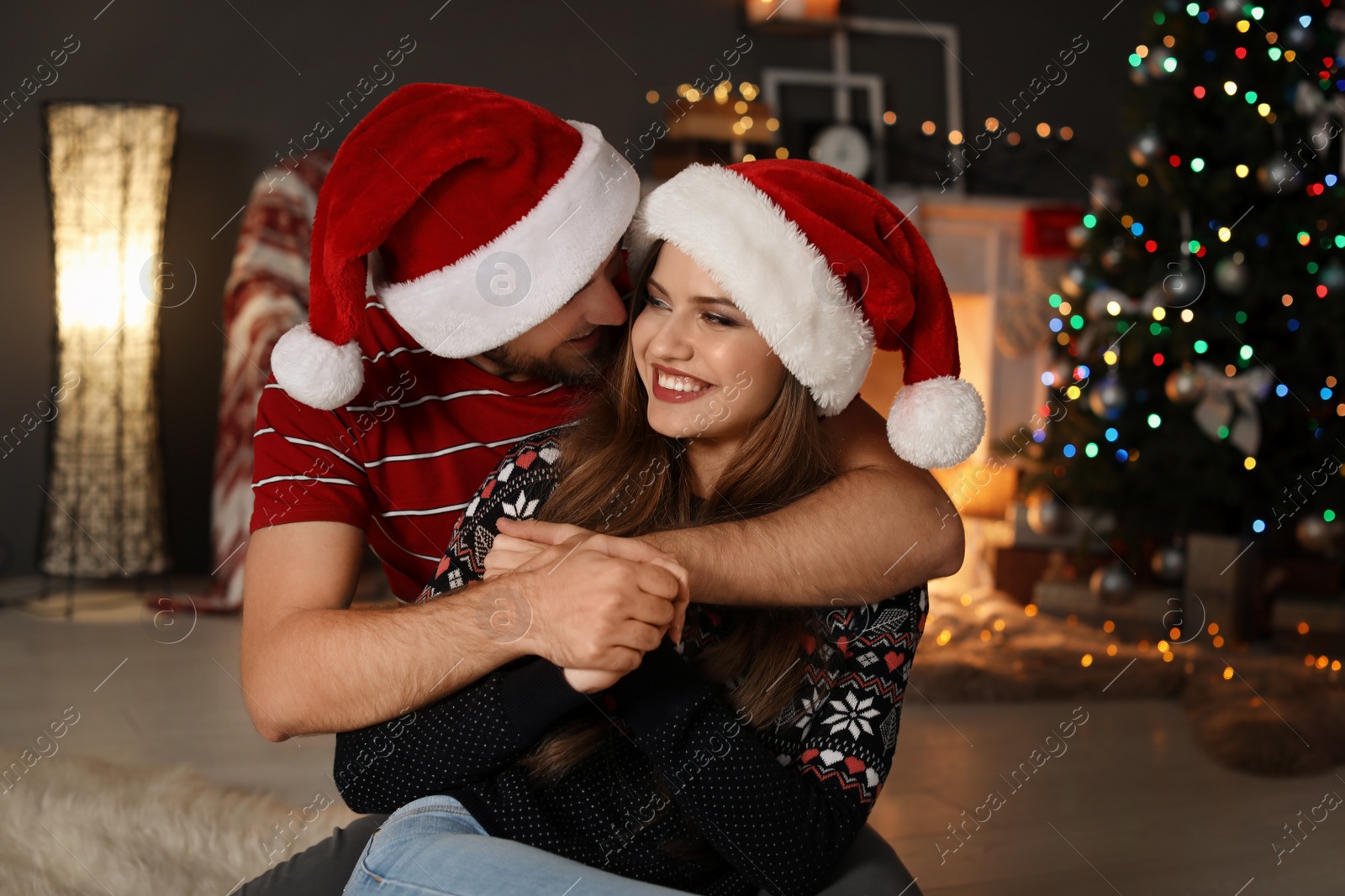 Photo of Happy young couple in Santa hats celebrating Christmas at home