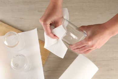 Photo of Woman wiping glass with paper towel at wooden table, top view