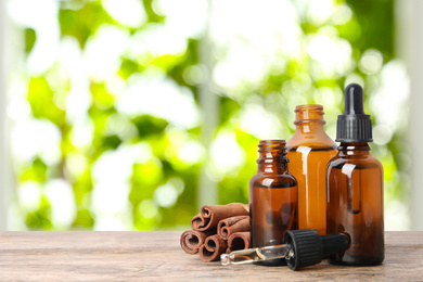 Bottles of essential oil and cinnamon sticks on wooden table against blurred background. Space for text