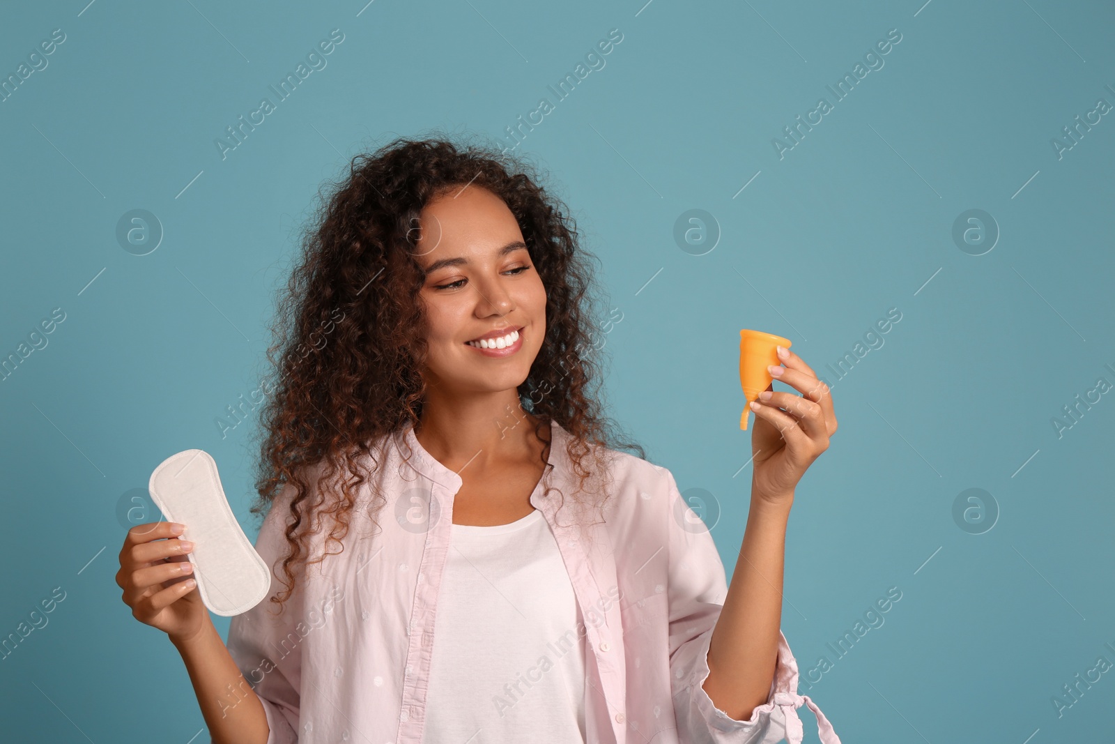 Photo of Young African American woman with menstrual cup and pantyliner on light blue background