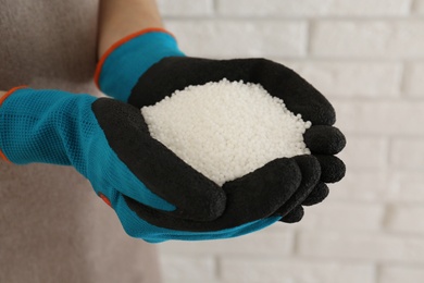 Photo of Woman holding pile of granular mineral fertilizer on blurred background, closeup