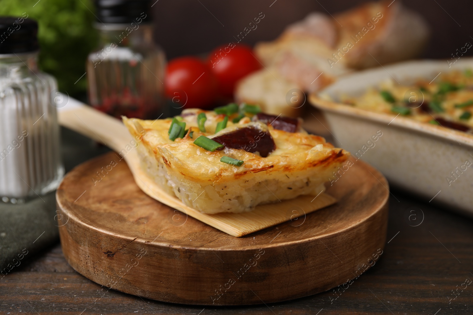 Photo of Spatula with piece of tasty sausage casserole on wooden table, closeup