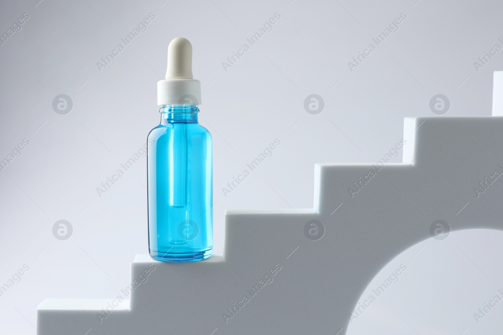 Photo of Bottle of luxury serum on stairs against white background