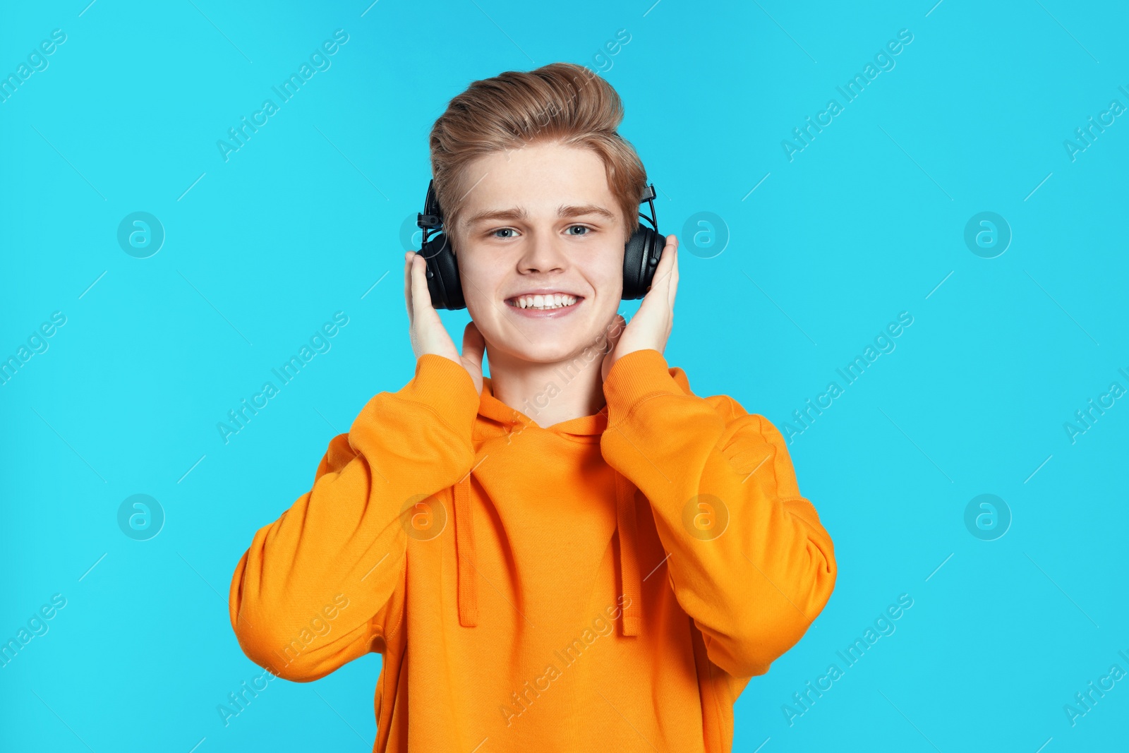 Photo of Teenage boy listening to music with headphones on light blue background