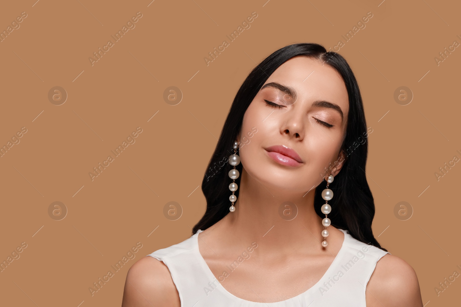 Photo of Young woman wearing elegant pearl earrings on brown background, space for text