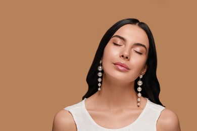 Young woman wearing elegant pearl earrings on brown background, space for text