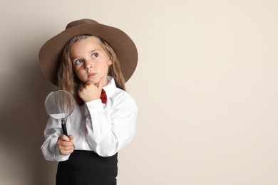 Cute little child in hat with magnifying glass playing detective on beige background, space for text