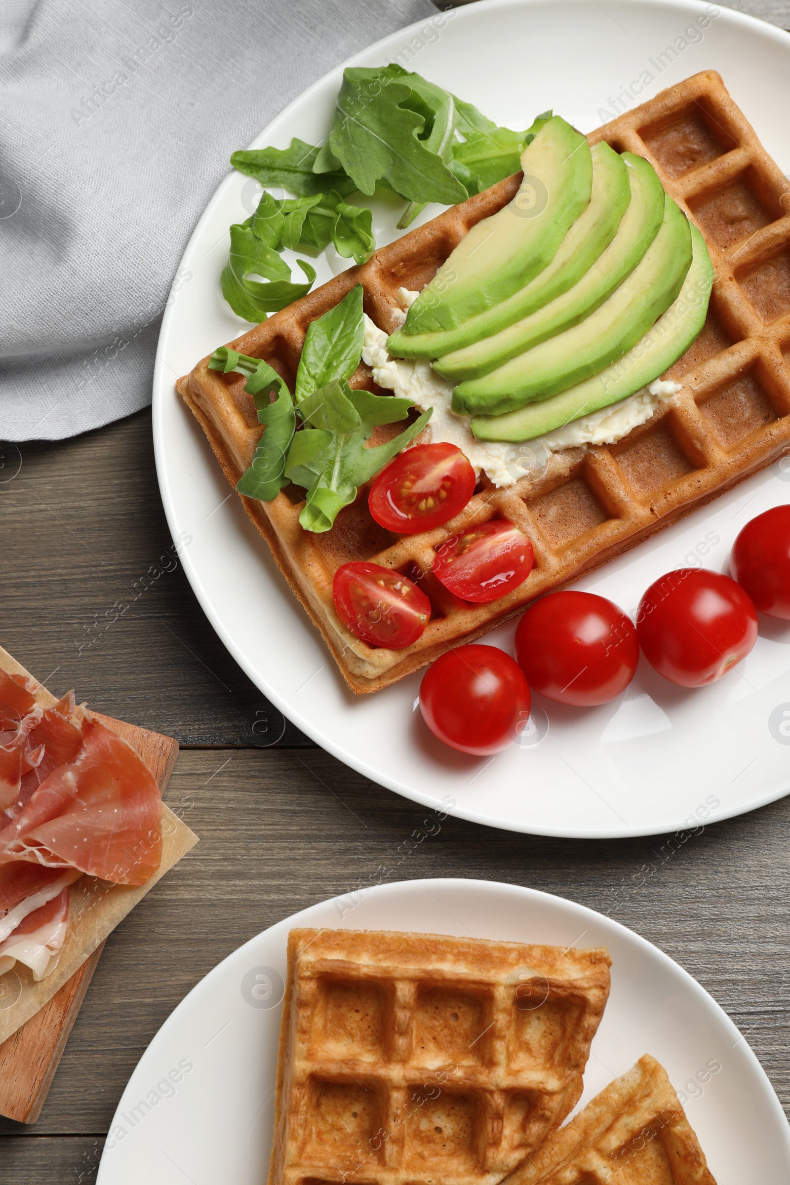 Photo of Fresh Belgian waffles with avocado, tomatoes and arugula on wooden table, flat lay