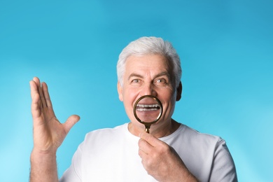 Mature man with healthy teeth and magnifier on color background