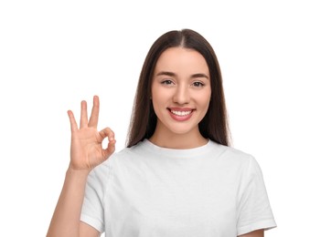Photo of Young woman with clean teeth smiling and showing ok gesture on white background