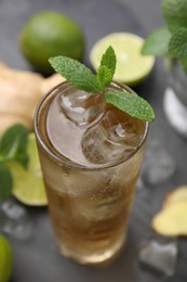Glass of tasty ginger ale with ice cubes and mint on grey wooden table, closeup