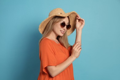 Photo of Beautiful young woman wearing straw hat and sunglasses on light blue background. Stylish headdress