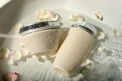 Photo of Hair care cosmetic products with flower petals and water in sink, above view