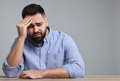 Portrait of sad man at wooden table on light grey background, space for text