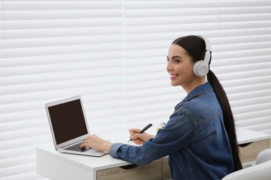 Photo of Woman in headphones studying on laptop indoors. Online translation course