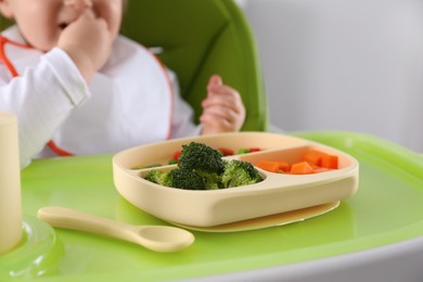 Photo of Little baby eating food in high chair, closeup