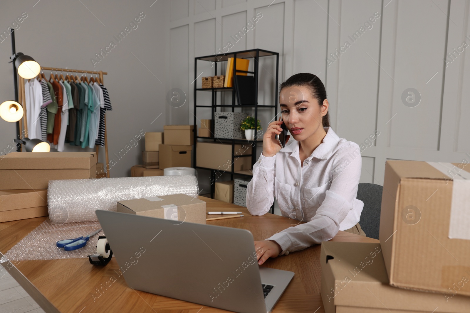 Photo of Seller talking on phone while working with laptop in office. Online store