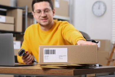 Photo of Seller with scanner and parcels at table in office, selective focus. Online store