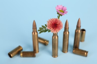 Photo of Bullets, cartridge cases and beautiful chrysanthemum flowers on light blue background