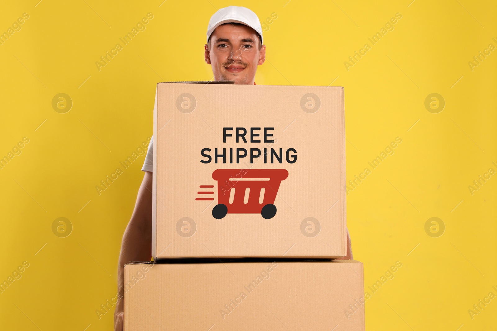 Image of Happy young courier with cardboard boxes on yellow background. Free shipping