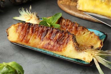 Plate with tasty grilled pineapple pieces and mint leaves on grey textured table, closeup