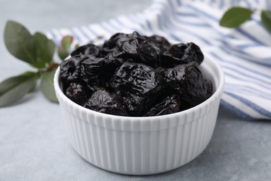 Sweet dried prunes in bowl on grey table, closeup